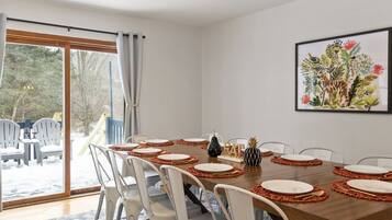 A dining area with a wooden table set for six, white chairs, and a large window with curtains.