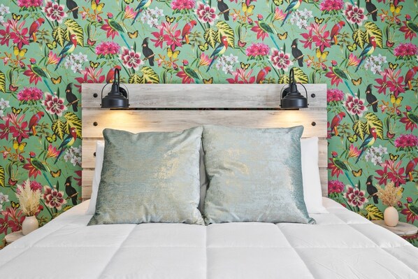 A bed with a wooden headboard, two pillows, and a floral wallpaper background.
