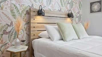 Een slaapkamer met een houten hoofdbord, twee bedlampjes, een bed met wit beddengoed, een klein tafeltje met een vaas en een wijnglas, en bloemenbehang.