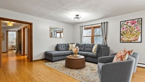 A modern living room with a grey sofa, a round ottoman, and a patterned rug.