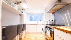 Une cuisine compacte équipée d’une cuisinière, d’un four et d’un évier, avec un plancher en bois et une fenêtre laissant entrer la lumière naturelle.