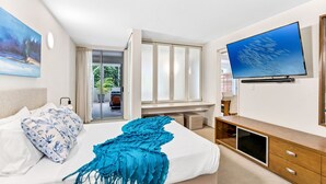 Una habitación de hotel moderna con cama, televisión, escritorio y balcón con vistas a zonas verdes.