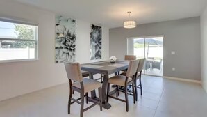 A spacious dining area with a large table and four chairs, two abstract paintings on the walls, and a view through a glass door to the outside. - Palm Breeze Lux Stay - Port St. Lucie (Port Saint Lucie)