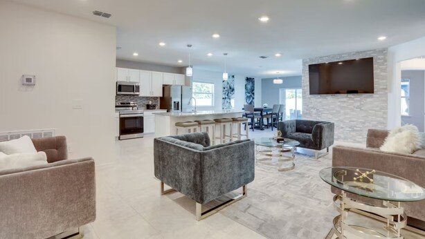 A modern living room with grey sofas, a glass coffee table, and a kitchen in the background. - Palm Breeze Lux Stay - Port St. Lucie (Port Saint Lucie)