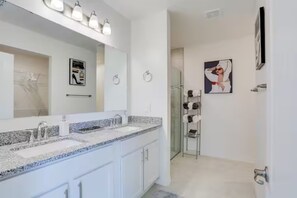 A modern bathroom with a double sink, a large mirror, and a shower area.