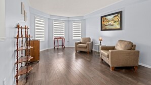 A room with hardwood flooring, a beige armchair, a sofa, a wooden sideboard, and a painting on the wall. - Sophisticated 2-Story Classic Home (Brampton)