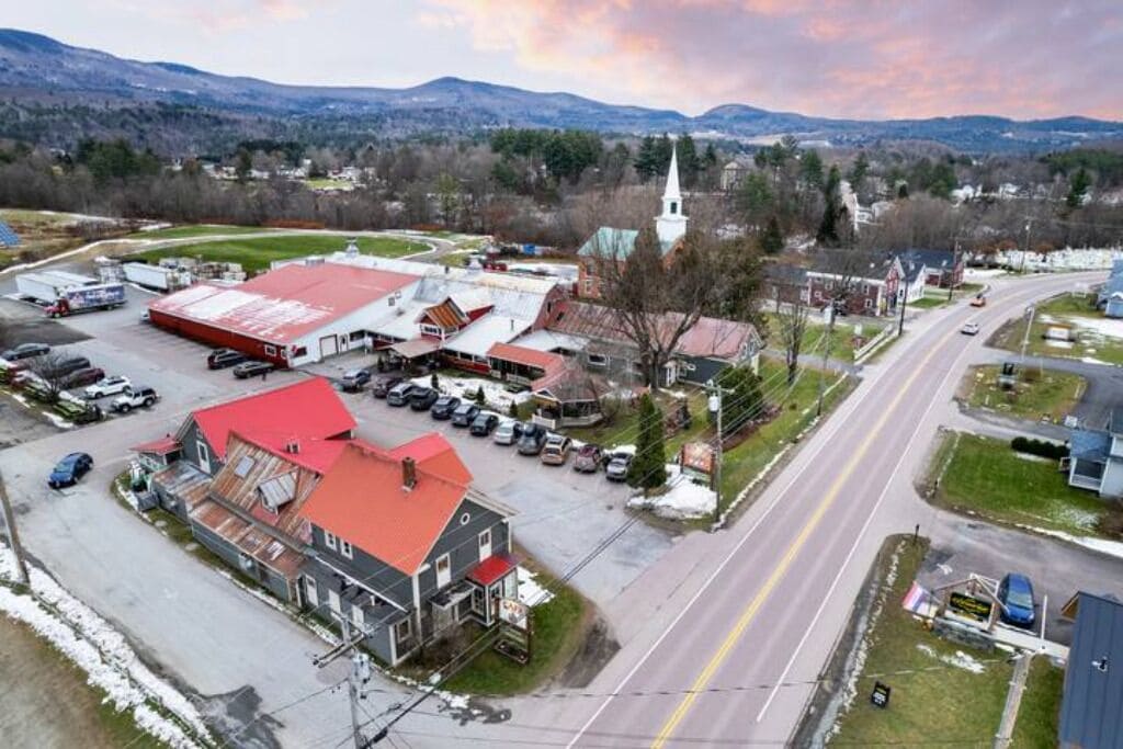 A commercial area with a large red-roofed building, a church with a white steeple, and a road with vehicles.
