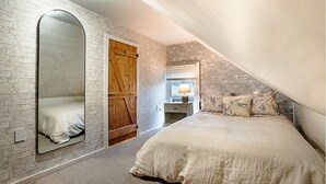 A bedroom with a large bed, a mirror, a wooden wardrobe, and a window with a lamp. - The Cider Loft (Waterbury)