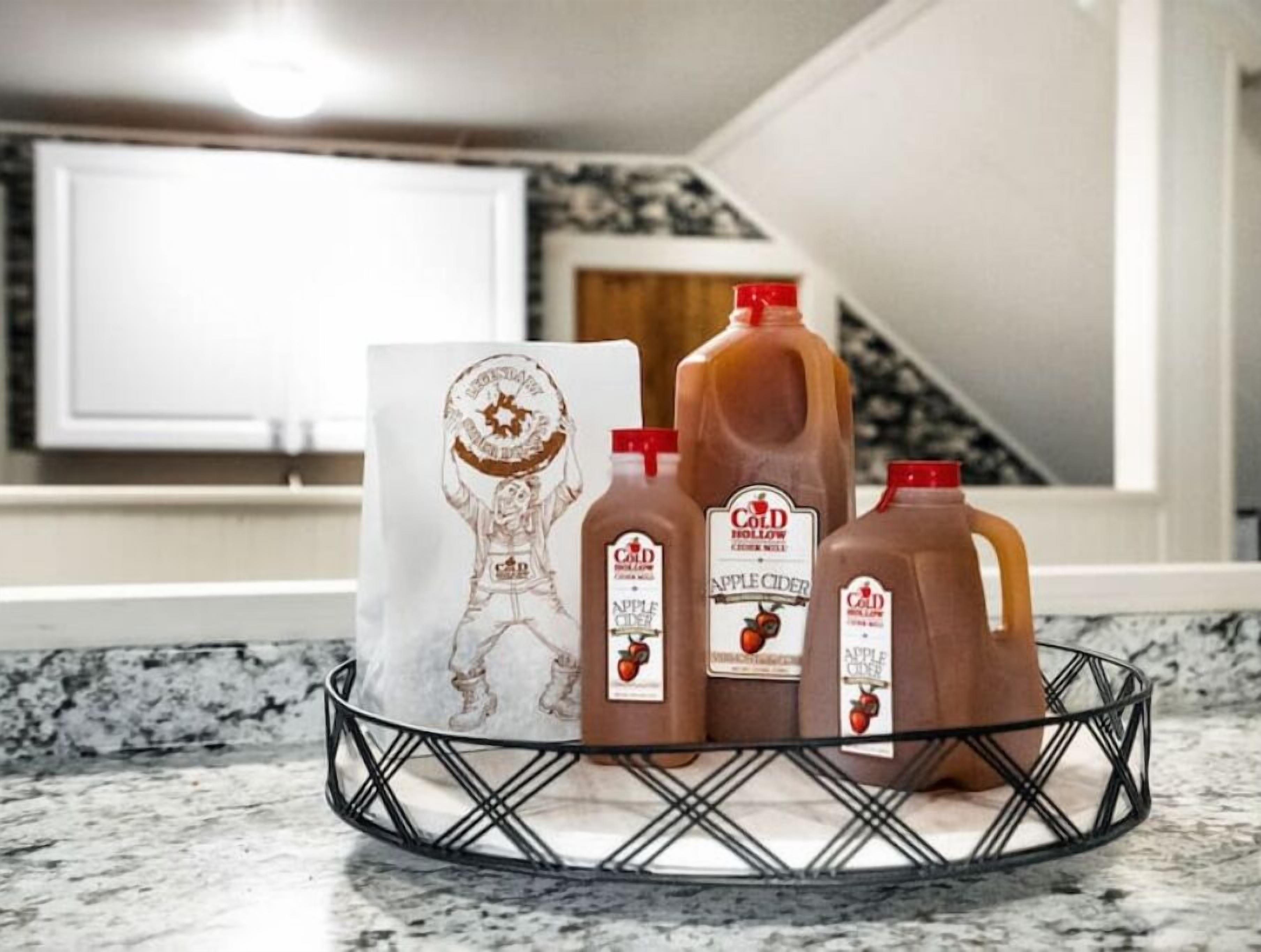 Una encimera de cocina con una cesta metálica que contiene tres botellas de sidra de manzana y una bolsa de papel con un logotipo.