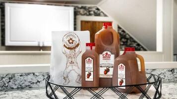 A kitchen counter with a metal basket containing three bottles of apple cider and a paper bag with a logo.