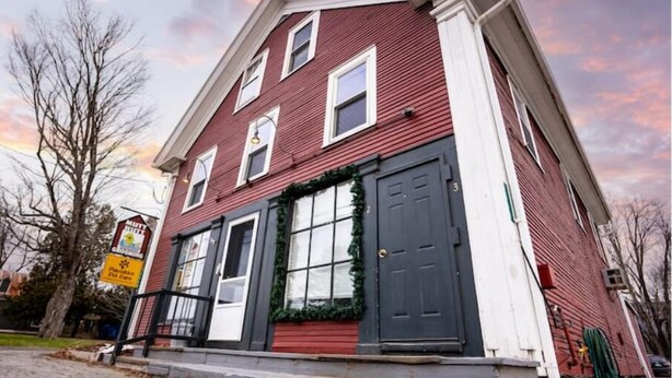 A two-story red building with a black front door, white trim, and a Christmas wreath. - The Cider Loft (Waterbury)