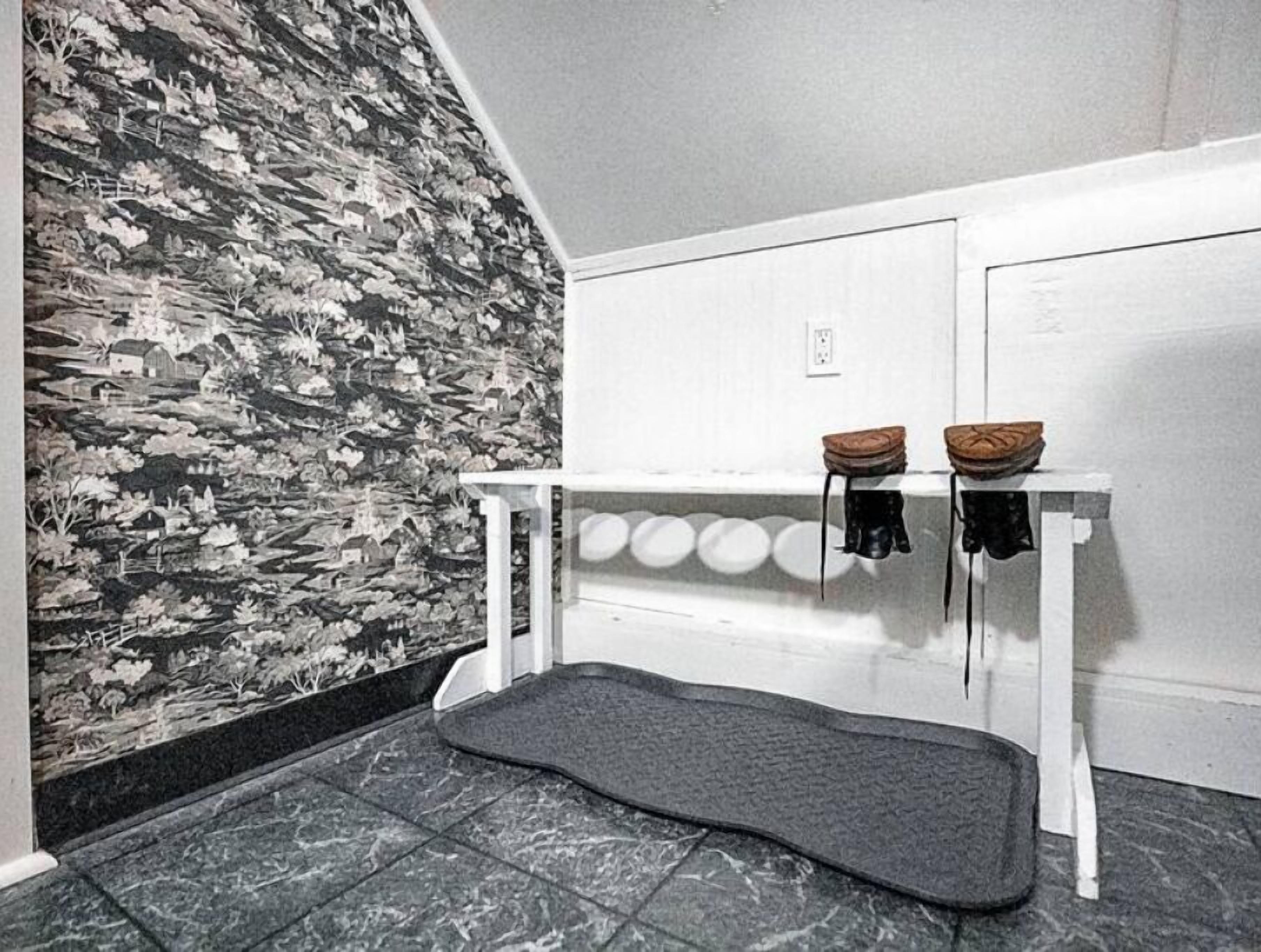 A bathroom with a patterned wallpaper, a white bench with a towel rack, and a grey mat on the floor.