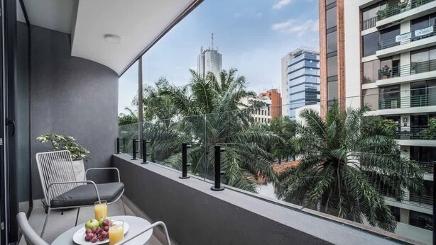 Un balcón con mesa, sillas y una bandeja de fruta y jugo.
