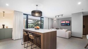 Una cocina moderna con una isla central, taburetes de bar, un amplio ventanal y un televisor de pantalla plana montado en la pared.