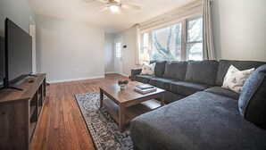 A living room with a dark grey sofa, a wooden coffee table, a flat-screen TV on a wooden stand, and a patterned rug.