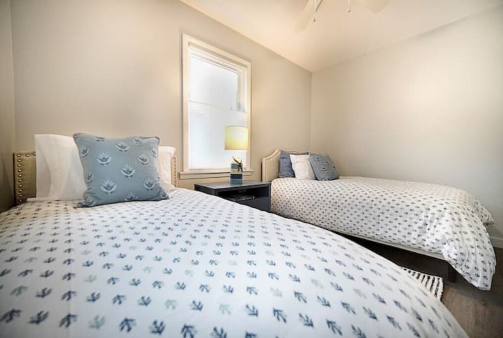 A bedroom with two beds, each with patterned bedding. There is a window with a view of the outside.