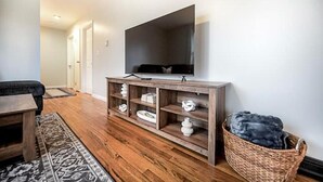 A living room with a flat-screen TV on a wooden stand, a patterned rug, and a wicker basket.