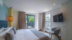 A modern hotel room with a large bed, a television, and a balcony with curtains. - E201 - Spacious 2-bed / 2-bath, A/C & Fast WiFi (Cali)