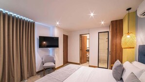 A modern bedroom with a large bed, a flat-screen TV mounted on the wall, a chair, and a door leading to another room. - E201 - Spacious 2-bed / 2-bath, A/C & Fast WiFi (Cali)