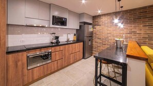 A modern kitchen with grey cabinets, a stainless steel oven, a microwave, and a refrigerator. There is a brick wall and a wooden countertop. - E103 - Brand-New Quiet & Comfortable Studio Unit (Cali)
