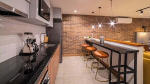 A modern kitchen with a brick wall backsplash, a black countertop, and three bar stools. - E103 - Brand-New Quiet & Comfortable Studio Unit (Cali)
