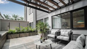 Une terrasse extérieure moderne, dotée d’une table en verre, de meubles en osier et de plantes en pot.