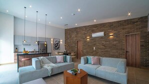 A modern living room with two light grey sofas, a wooden coffee table, and a kitchen area with a brick wall and pendant lighting. - E302 - Luxurious Top Floor Apartment with Terrace (Cali)