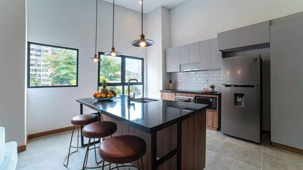 A modern kitchen with a large island, bar stools, stainless steel appliances, and a view of the city through a large window. - E302 - Luxurious Top Floor Apartment with Terrace (Cali)