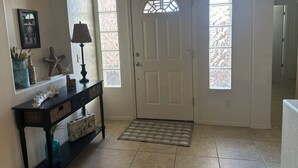 A hallway with a white door, a console table with decorative items, a patterned rug, and a tiled floor. - 2-bedroom clean home in Sierra Vista, WiFi, AC, covered patio & shaded backyard. (Sierra Vista)