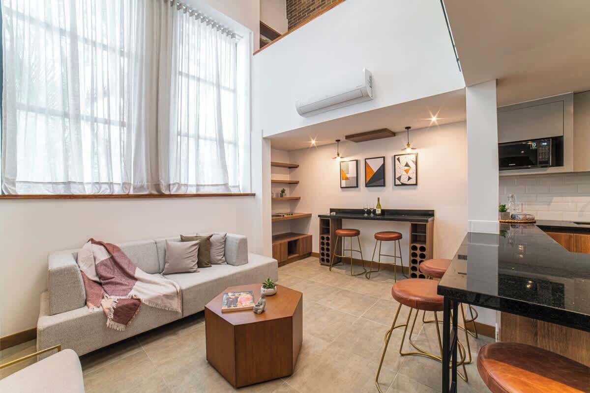 Un apartamento moderno con sala de estar que incluye un sofá, una mesa de centro y un comedor con una mesa negra y taburetes.