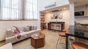 Eine moderne Wohnung mit Wohnbereich, ausgestattet mit einer Couch, einem Couchtisch und einem Essbereich mit einem schwarzen Tisch und Hockern.