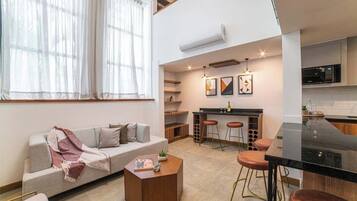 Un apartamento moderno con sala de estar que incluye un sofá, una mesa de centro y un comedor con una mesa negra y taburetes.