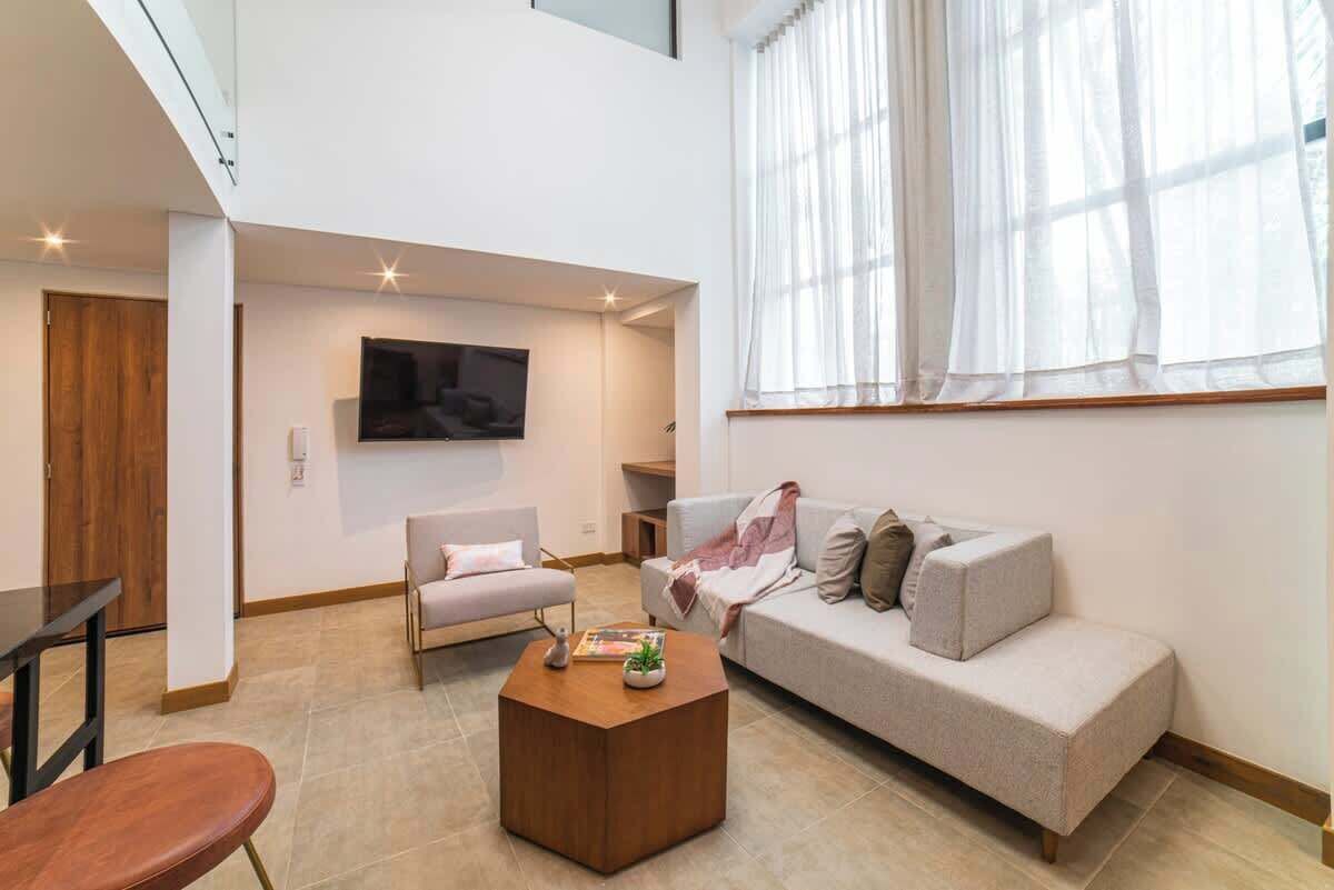 Una sala de estar moderna con sofá, sillón, mesa de centro y televisión montada en la pared.