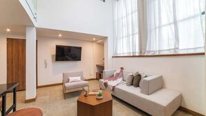 Ein modernes Wohnzimmer mit Sofa, Sessel, Couchtisch und einem an der Wand befestigten Fernseher.