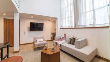 Una sala de estar moderna con sofá, sillón, mesa de centro y televisión montada en la pared.