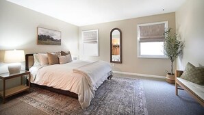 Quarto com cama, mesa de cabeceira, abajur e uma grande janela com vista.