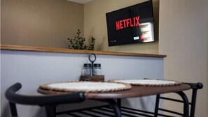 Uma cozinha com duas formas redondas para assar em uma mesa de madeira, uma cadeira preta e uma televisão fixada na parede exibindo 'NETFLIX'.