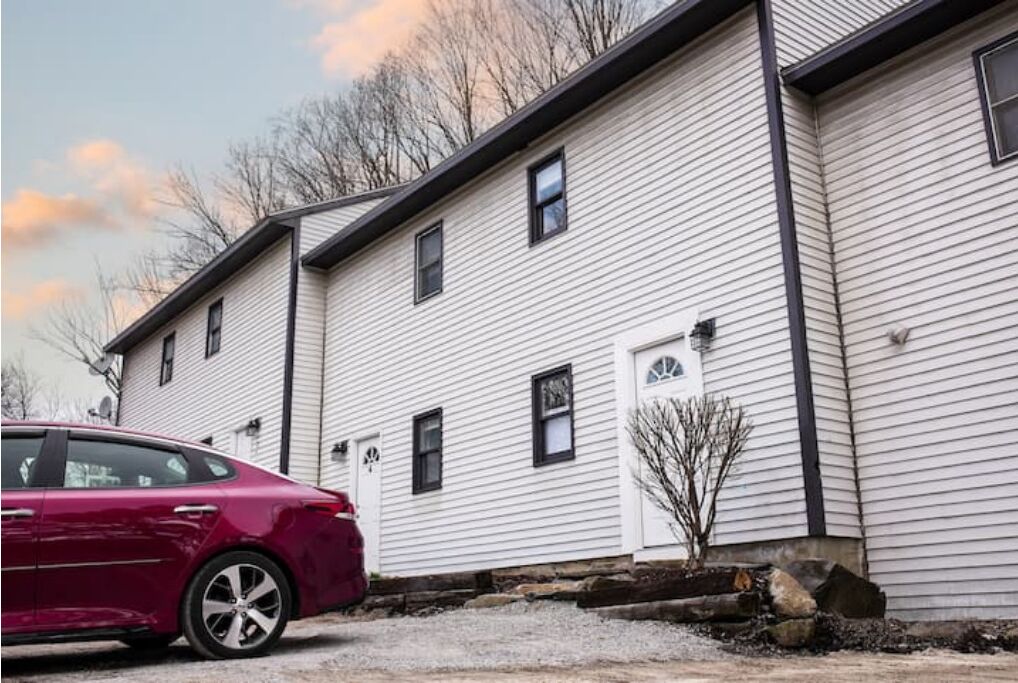 A two-story white building with a red car parked in front.