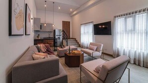 A modern living room with a sofa, armchair, coffee table, and artwork on the wall.