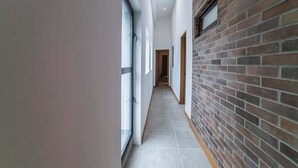 A narrow hallway with a tiled floor, a brick wall on one side, and a glass door on the other.