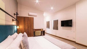 A hotel room with a large bed, a desk with a chair, a TV mounted on the wall, and a wooden wardrobe.