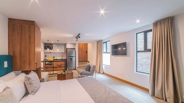 A modern hotel room with a large bed, a kitchenette, a seating area, and a large window with curtains. - E204 - Cozy Studio, Fast WiFi, A/C, Hot Water (Cali)