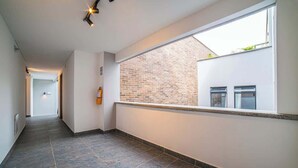 A corridor with a tiled floor, a window with a view of a brick wall and a window, and a light fixture on the ceiling. - E204 - Cozy Studio, Fast WiFi, A/C, Hot Water (Cali)