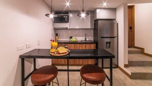 A modern kitchen with a black countertop, two brown leather bar stools, a stainless steel refrigerator, and a microwave above the counter. - E204 - Cozy Studio, Fast WiFi, A/C, Hot Water (Cali)