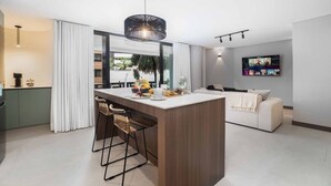 A modern kitchen with a central island, bar stools, a hanging light fixture, and a flat-screen TV mounted on the wall. - Hygge 301 - 2-Bed Beauty | Balcony | Near Granada (Cali)
