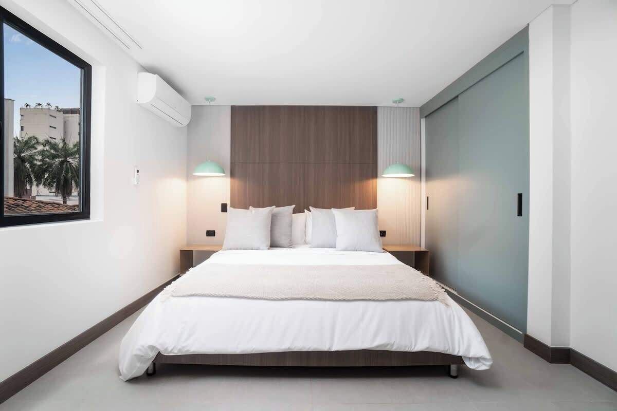 Camera da letto moderna con un letto grande, due abat-jour, una testiera in legno e una finestra con vista sulle palme.
