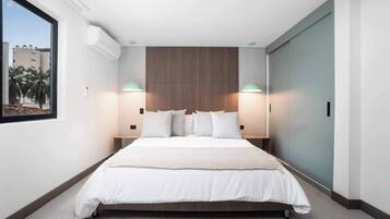Camera da letto moderna con un letto grande, due abat-jour, una testiera in legno e una finestra con vista sulle palme.