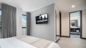 Une chambre d’hôtel moderne avec un grand lit, un téléviseur fixé au mur affichant l’interface Netflix, et une vue sur la salle de bain par une porte ouverte.