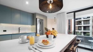 Una cocina moderna con una isla central, un comedor con sillas y vistas a un edificio residencial.