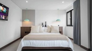 Un dormitorio de hotel moderno con una cama grande, dos mesitas de noche, un televisor y un ventanal con cortinas.